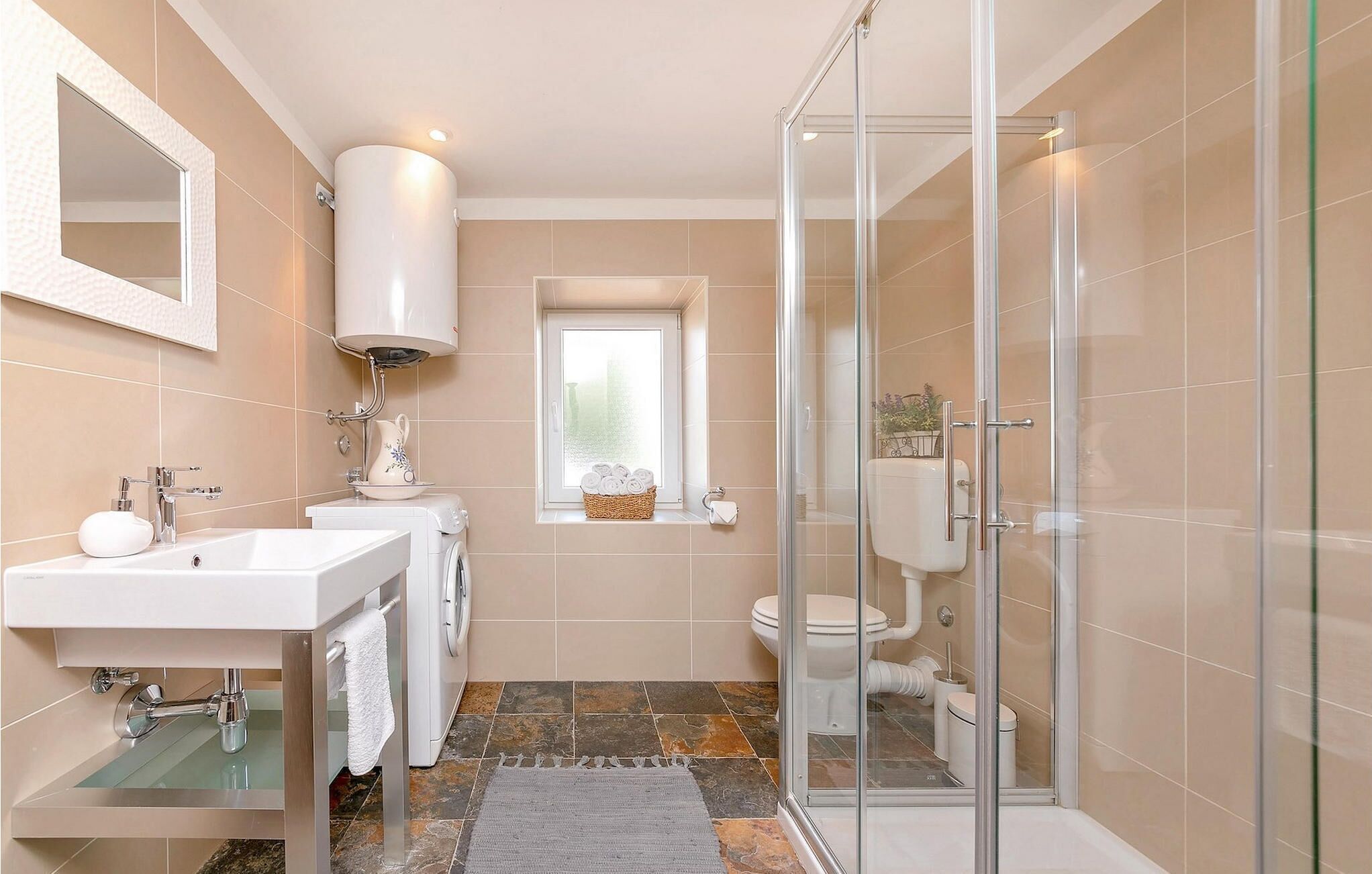 Ein modernes Badezimmer mit Duschkabine aus Glas, einem Waschbecken, einer Toilette und einem Fenster.