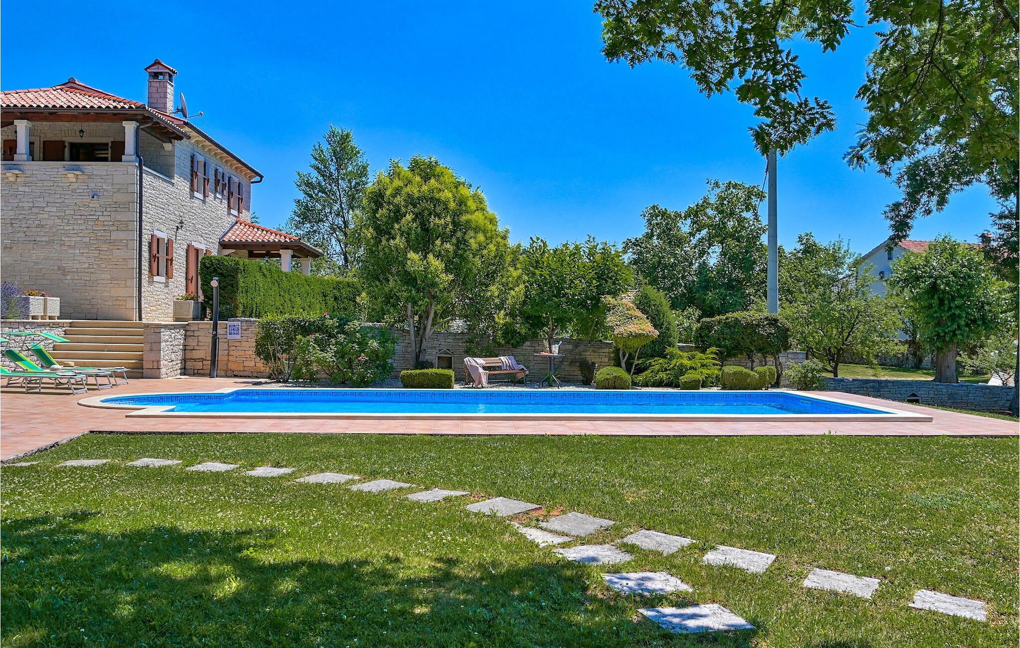 Ein Swimmingpool mit Liegestühlen, ein Steinhaus und ein gepflegter Garten.