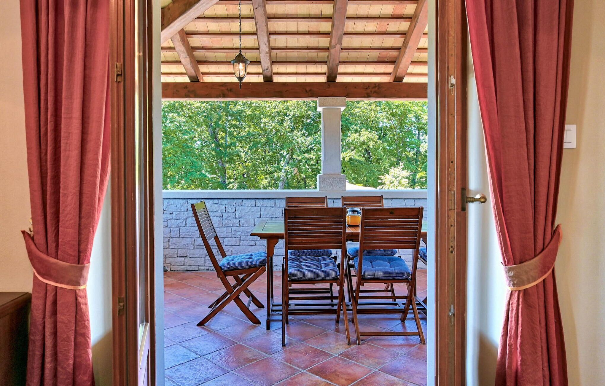 Un patio descubierto con una mesa y sillas de madera, un muro de piedra y vistas a zonas verdes.