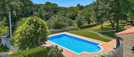 A rectangular swimming pool with a stone border, surrounded by a well-maintained lawn and trees.