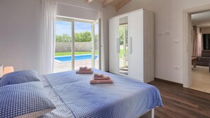 Ein Schlafzimmer mit Bett, Blick auf einen Swimmingpool und einer Schiebetür, die auf einen Balkon führt.