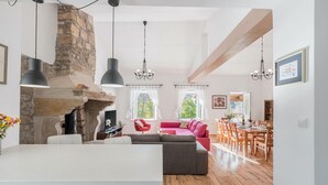 A spacious living area with a stone fireplace, a red sofa, and a dining area with wooden furniture. - Gorgeous home in Boljun (Boljun)
