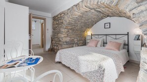 A bedroom with a stone archway, a bed with floral bedding, a white chair with magazines, and a small table. - Gorgeous home in Boljun (Boljun)
