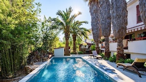 A swimming pool surrounded by bamboo and palm trees, with lounge chairs and a pergola.