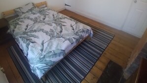 A bedroom with a bed, a wooden headboard, a striped rug, and a door with a handle.