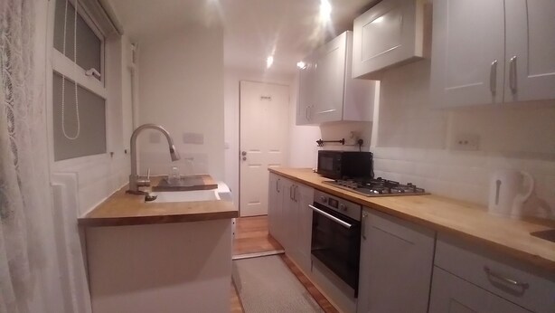 A compact kitchen with white cabinets, a wooden countertop, a sink, a microwave, and an oven.