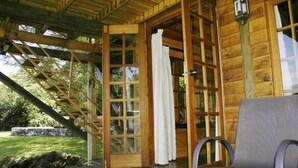 A wooden cabin with a covered porch, a set of stairs leading to a glass door, and a chair on the porch.
