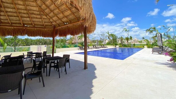 A poolside area with a thatched roof, lounge chairs, and a swimming pool. - ALDEA TULUM (Tulum)