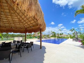 A poolside area with a thatched roof, lounge chairs, and a swimming pool. - ALDEA TULUM (Tulum)
