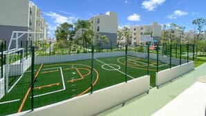 A basketball court with a net, surrounded by a fence, and adjacent to residential buildings. - ALDEA TULUM (Tulum)