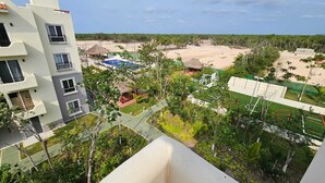 A high-rise building with multiple balconies overlooking a beach area with a pool, tennis court, and a thatched-roof structure. - ALDEA TULUM (Tulum)
