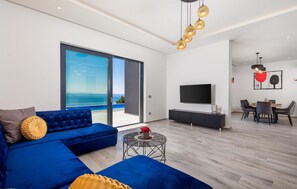 Una sala de estar moderna con un sofá azul, un televisor de pantalla plana y un comedor con sillas y una mesa.