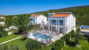 Une villa moderne à deux étages, dotée d’une piscine, entourée d’une végétation luxuriante et avec des collines en arrière-plan.