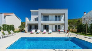 Une maison moderne à deux étages dotée d’une piscine, d’un espace salon extérieur et d’un jardin.