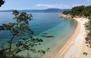 Une plage à l’eau turquoise et limpide, bordée d’un rivage sablonneux, avec une chaîne de montagnes en toile de fond.
