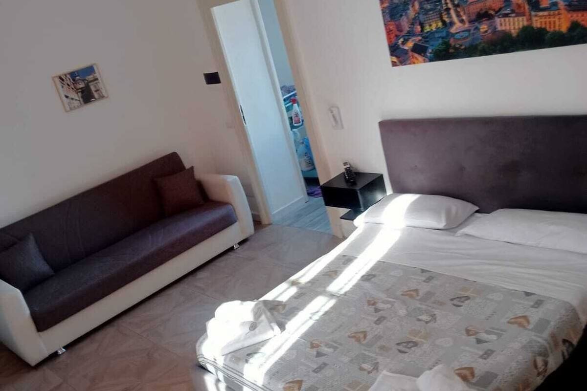 A bedroom with a bed, a sofa, a painting on the wall, and a door leading to another room.
