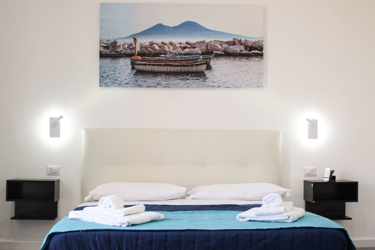 A hotel room with a large bed, two bedside tables, and a wall-mounted painting of a boat on water.