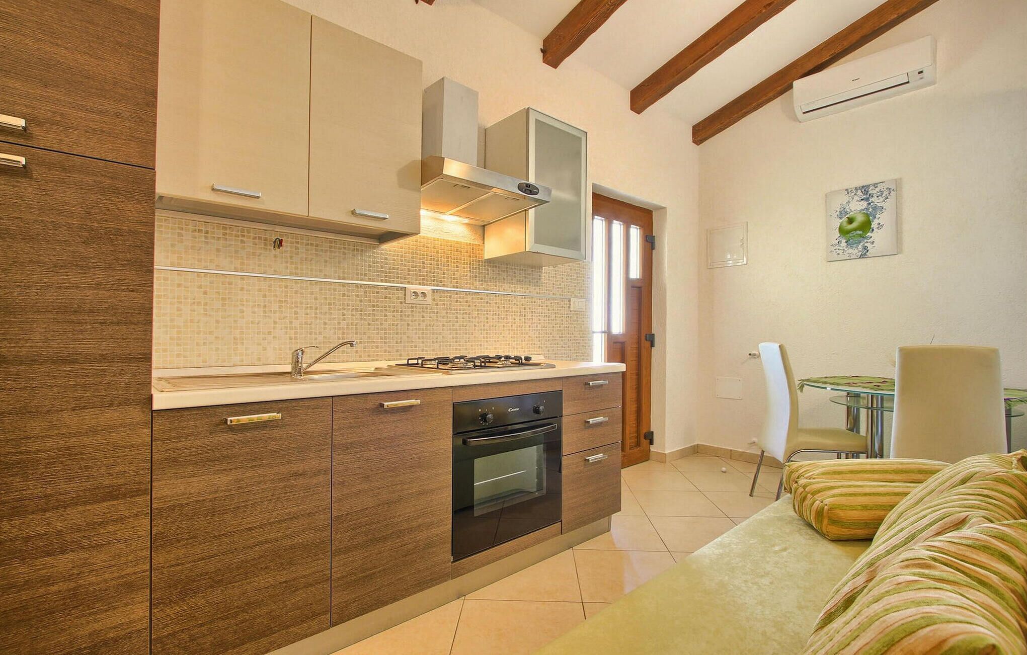 Une cuisine compacte équipée d’un four encastré, d’une cuisinière à gaz et d’un four à micro-ondes. Un coin repas avec une table et des chaises est également disponible.