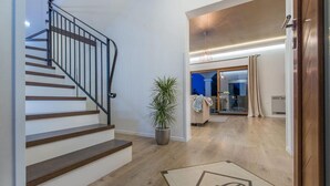 Un intérieur moderne avec un escalier en bois, une plante en pot et une porte ornée d’un motif géométrique.