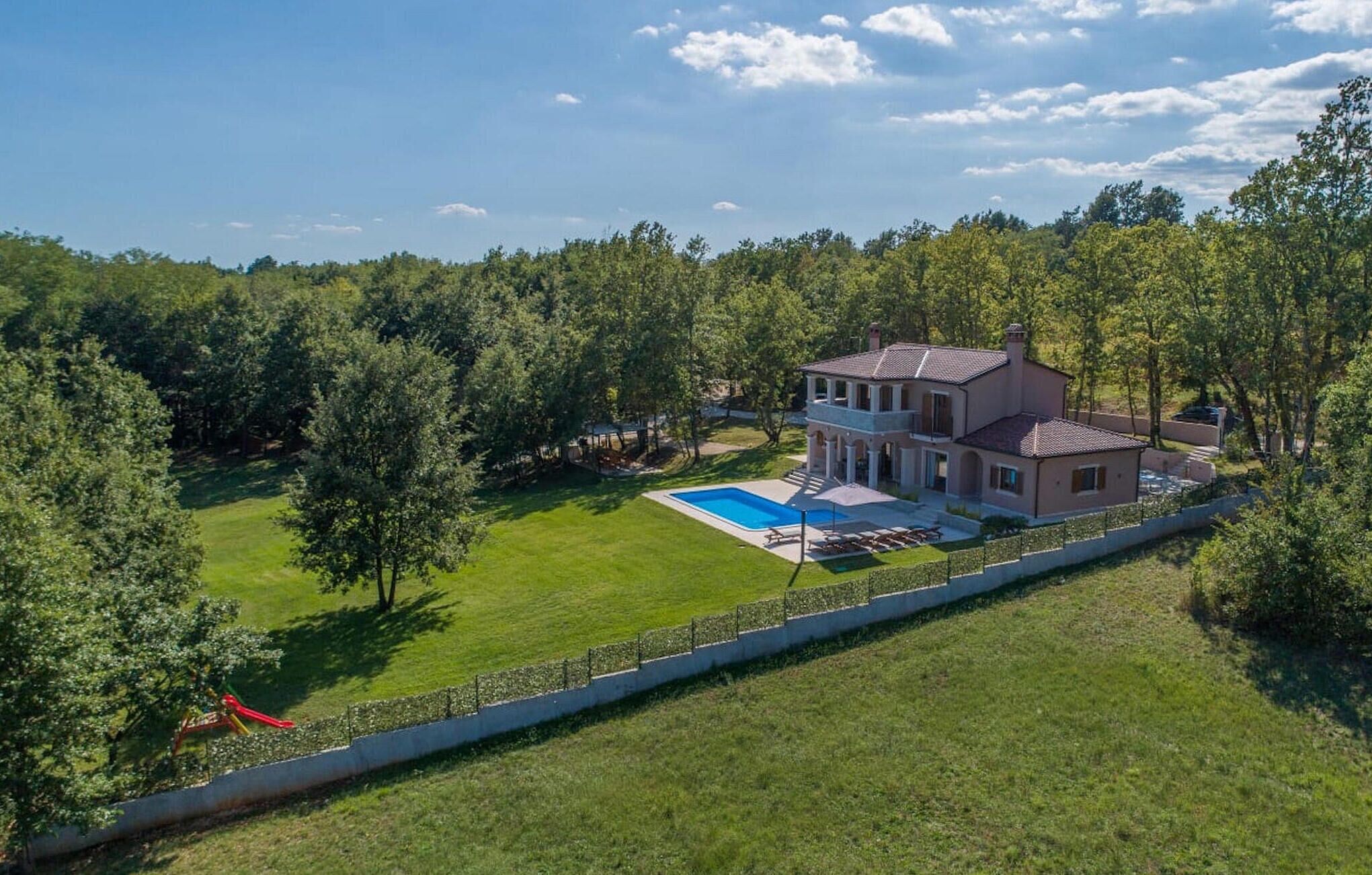 Ein großes, zweistöckiges Haus mit Swimmingpool, umgeben von einem gepflegten Rasen und Bäumen.