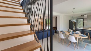A modern interior with a wooden staircase, a dining area with a long table and chairs, and a kitchen with a stove and cabinets.