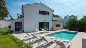 A modern two-story house with a swimming pool, outdoor seating, and a stone wall.