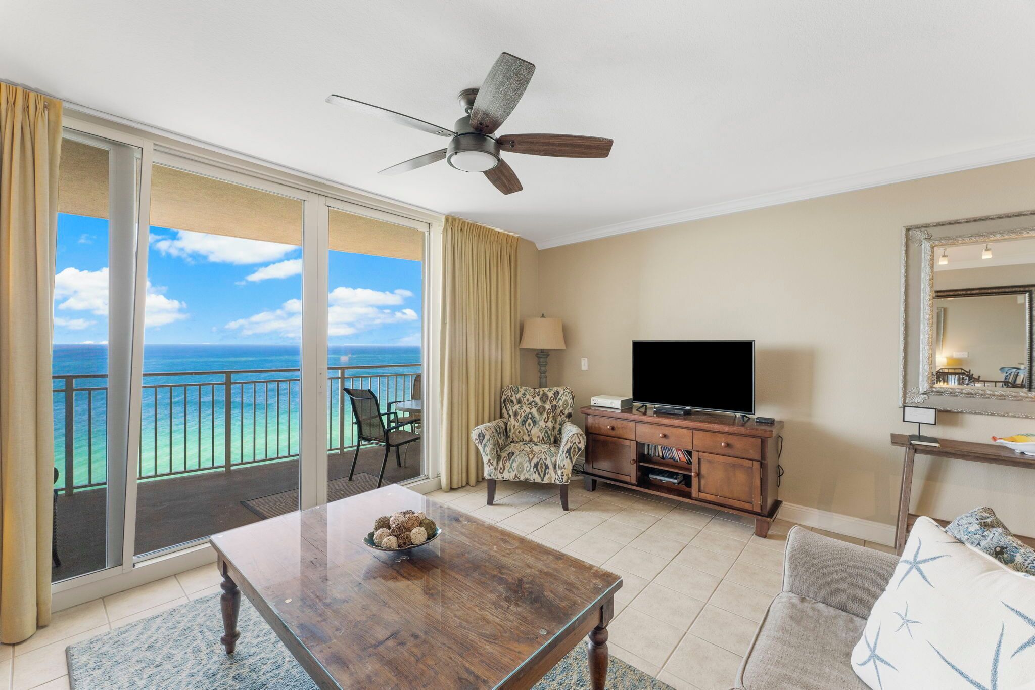 A room with a balcony, a television, a patterned armchair, a wooden coffee table, and a sofa.