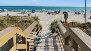 A wooden boardwalk leading to a sandy beach with umbrellas and people. - Emerald Beach Resort 2235 (Panama City Beach)