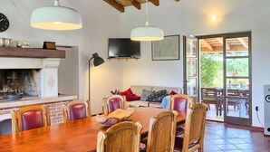 A dining area with a wooden table, chairs, and pendant lights. There is a fireplace, a television, and a view of the outdoors through a glass door. - Lovely home in Rovinj (Rovinj)