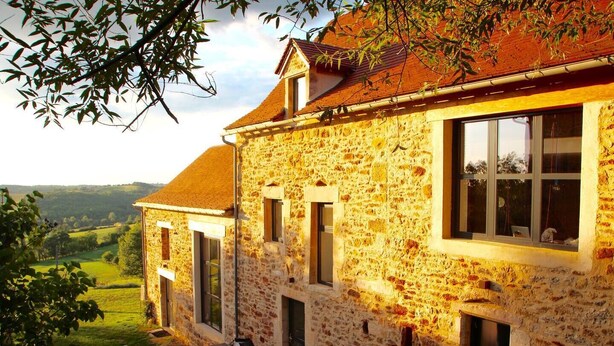 A stone building with multiple windows and a red roof, surrounded by greenery and a hilly landscape. - Maison DE Charme, 2 Pigeonniers ET Piscine (Saint-Rémy)