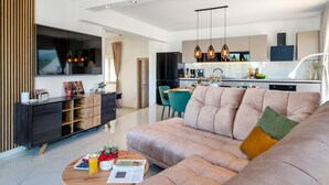 A modern living room with a large sofa, a coffee table, and a TV. There is a kitchen in the background with a dining area. - Stunning home in Sibenik (Sibenik)