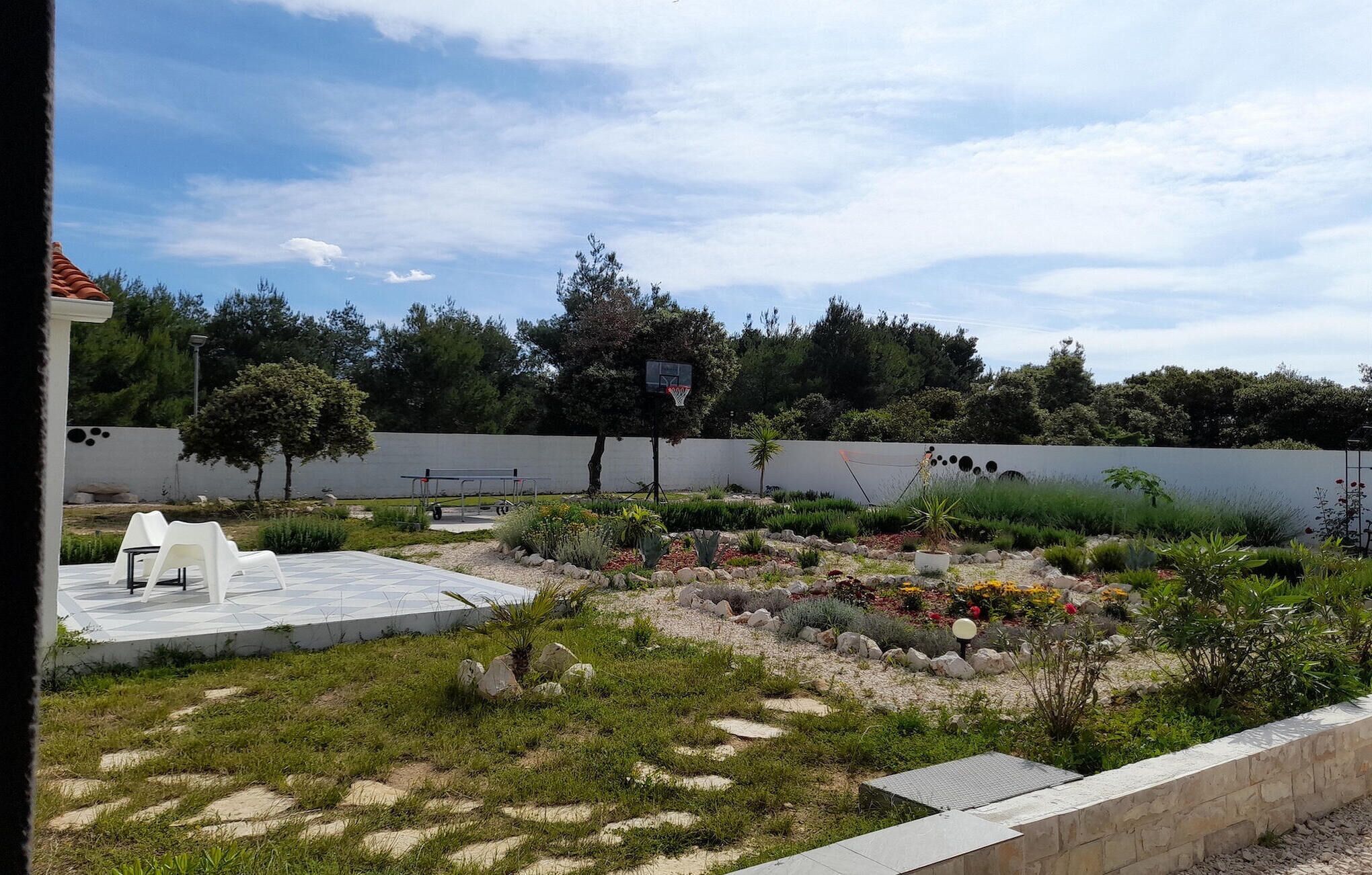 A landscaped garden with a basketball hoop, seating area, and a variety of plants and rocks.