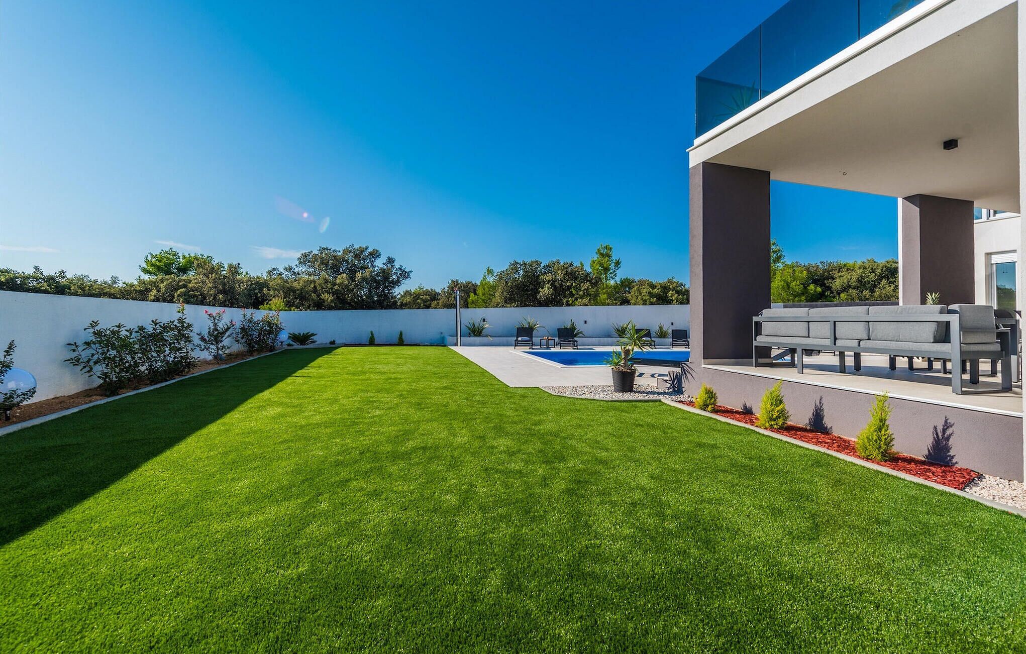 A modern outdoor patio with a pool, seating area, and well-maintained lawn.