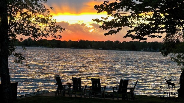A lakeside view with a sunset, chairs, and a moose statue. - Relax at the Lake Osakis Getaway. Fireplace, Lake Views & Winter Fun. Sleeps 10 (Osakis)