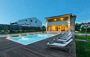 Una piscina exterior moderna con tumbonas y un muelle de madera.