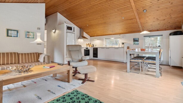 Eine moderne Küche mit weißen Schränken, ein Essbereich mit Tisch und Stühlen sowie ein Wohnzimmer mit Sofa und Couchtisch.