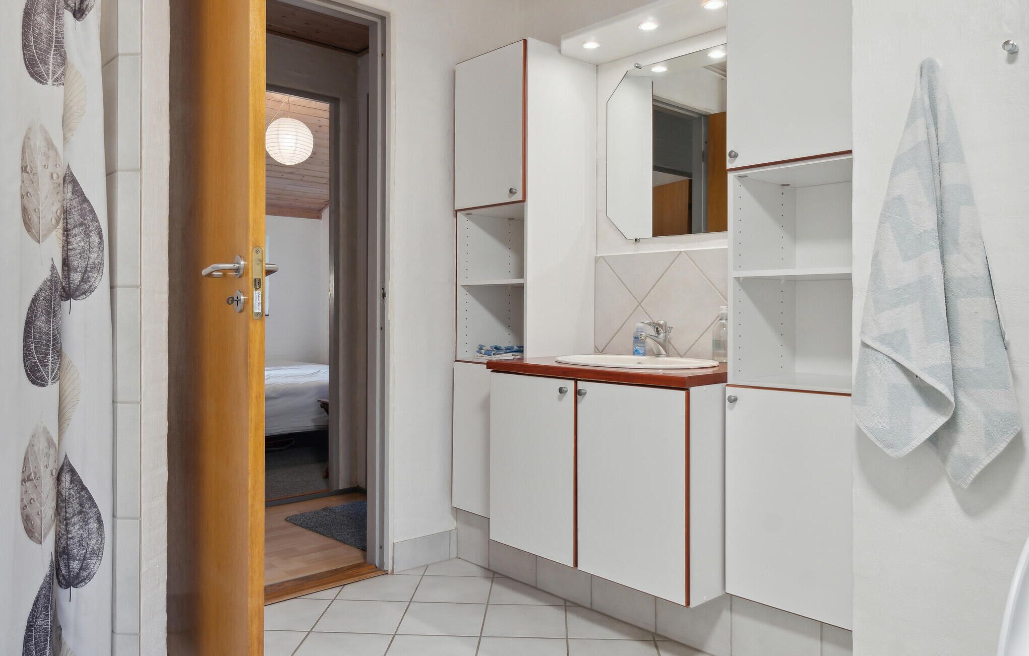 A modern bathroom with white cabinetry, a wooden countertop, a mirror, and a towel hanging on the wall.