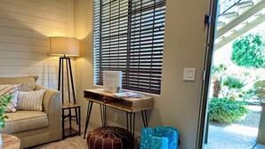 Un salon chaleureux avec un canapé, une lampe sur pied, une petite table en bois sur laquelle repose un livre, un tapis à motifs et une fenêtre avec des stores.