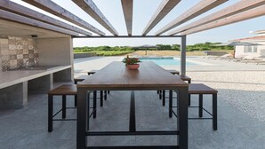 An outdoor dining area with a pool view, featuring a long table and benches, surrounded by a pergola structure. - Gorgeous home in Kanfanar (Kanfanar)