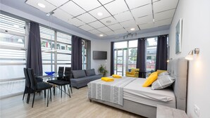 A modern hotel room with a large bed, a desk, and a chair. There are windows with curtains, a flat-screen TV, and a potted plant. - Stunning apartment in Kastel Novi with WiFi (Kastel Novi)