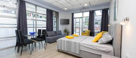 Una habitación de hotel moderna con una cama grande, un escritorio y una silla. Hay ventanas con cortinas, un televisor de pantalla plana y una planta en maceta.