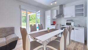 Une cuisine moderne avec des meubles blancs, une table à manger avec des chaises et une vue sur l’extérieur.