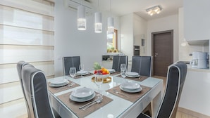 Un coin repas avec une table en verre, des chaises noires et un centre de table composé d’un saladier de fruits.