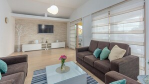 Un salon moderne avec un canapé marron, une table basse en verre et un téléviseur fixé sur un mur en briques.