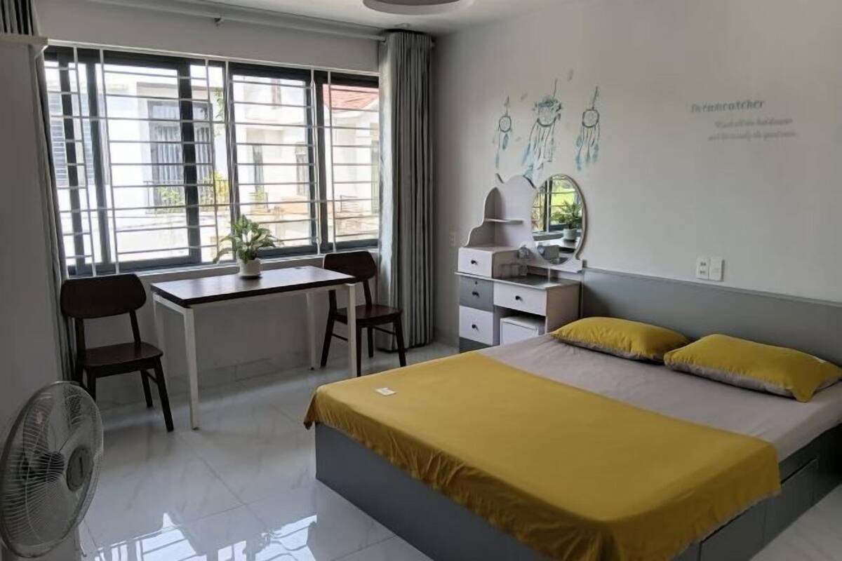 A bedroom with a bed, a desk, a chair, a mirror, and a window.