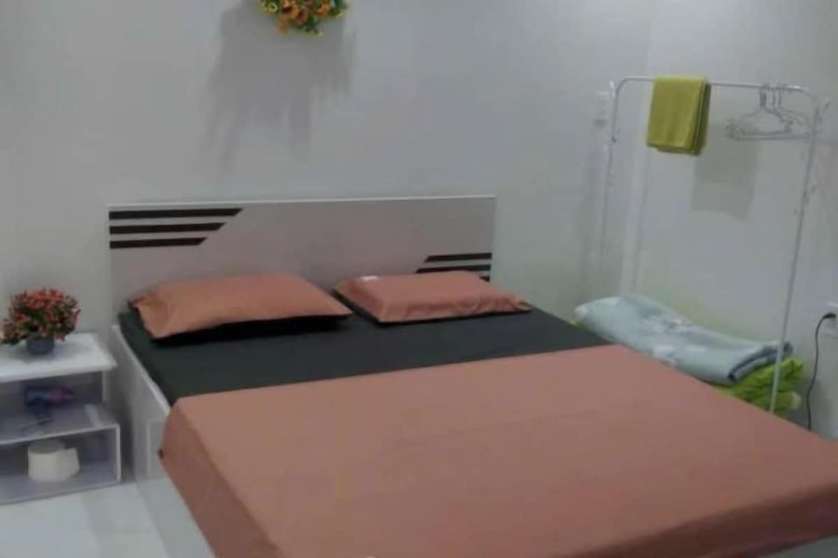A bedroom with a bed, a bedside table, a hanging towel, and a wall-mounted shelf with a plant.