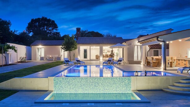 Una casa moderna amb piscina, zona d'estar a l'aire lliure i un pati ben il·luminat.