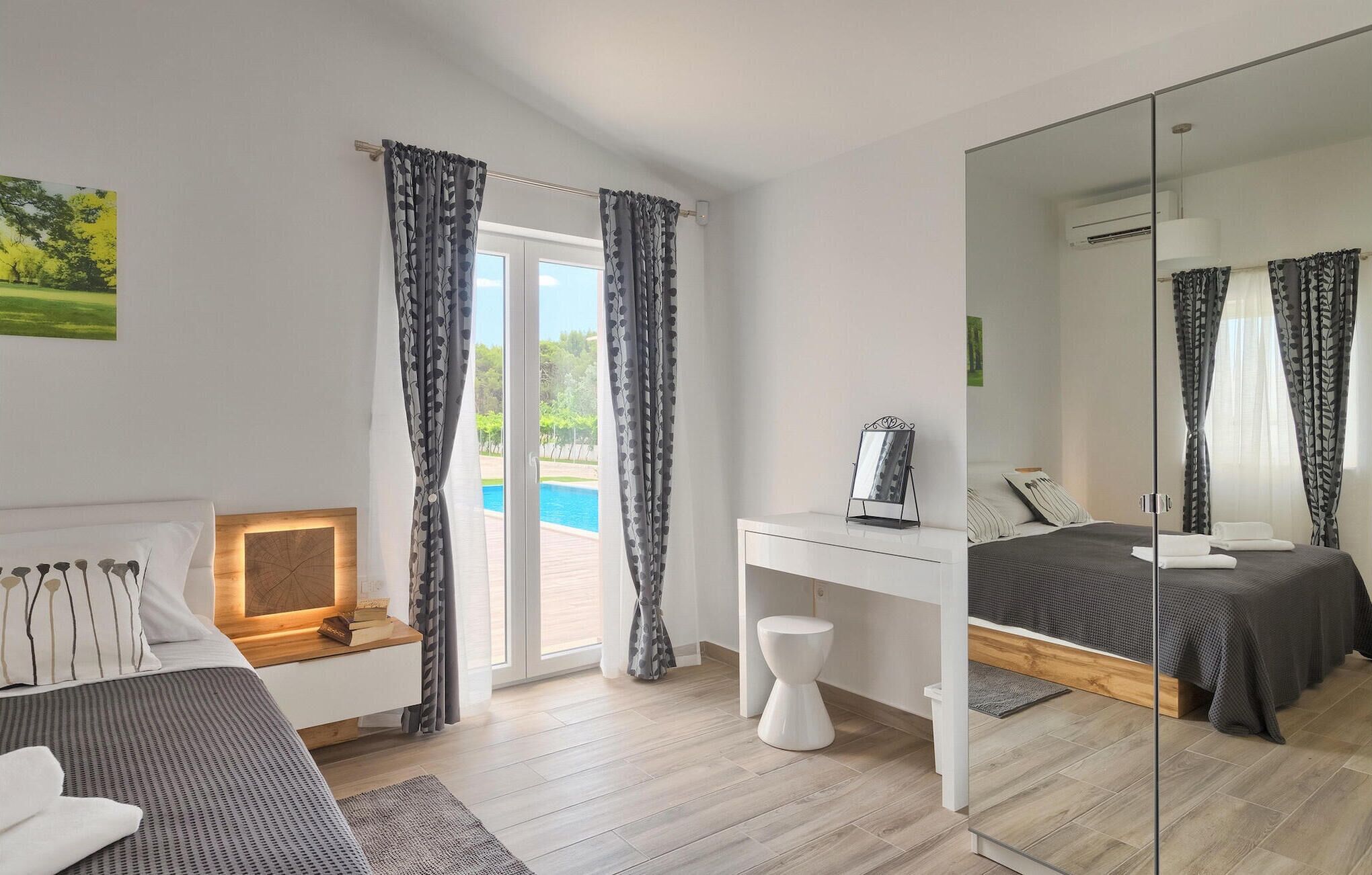 A modern bedroom with a bed, a desk, a mirror, and a view of a swimming pool.