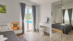 Un dormitori modern amb un llit, una taula de treball, un mirall i vista a una piscina.