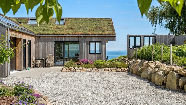Una casa moderna con techo verde, camino de grava y vista al mar.
